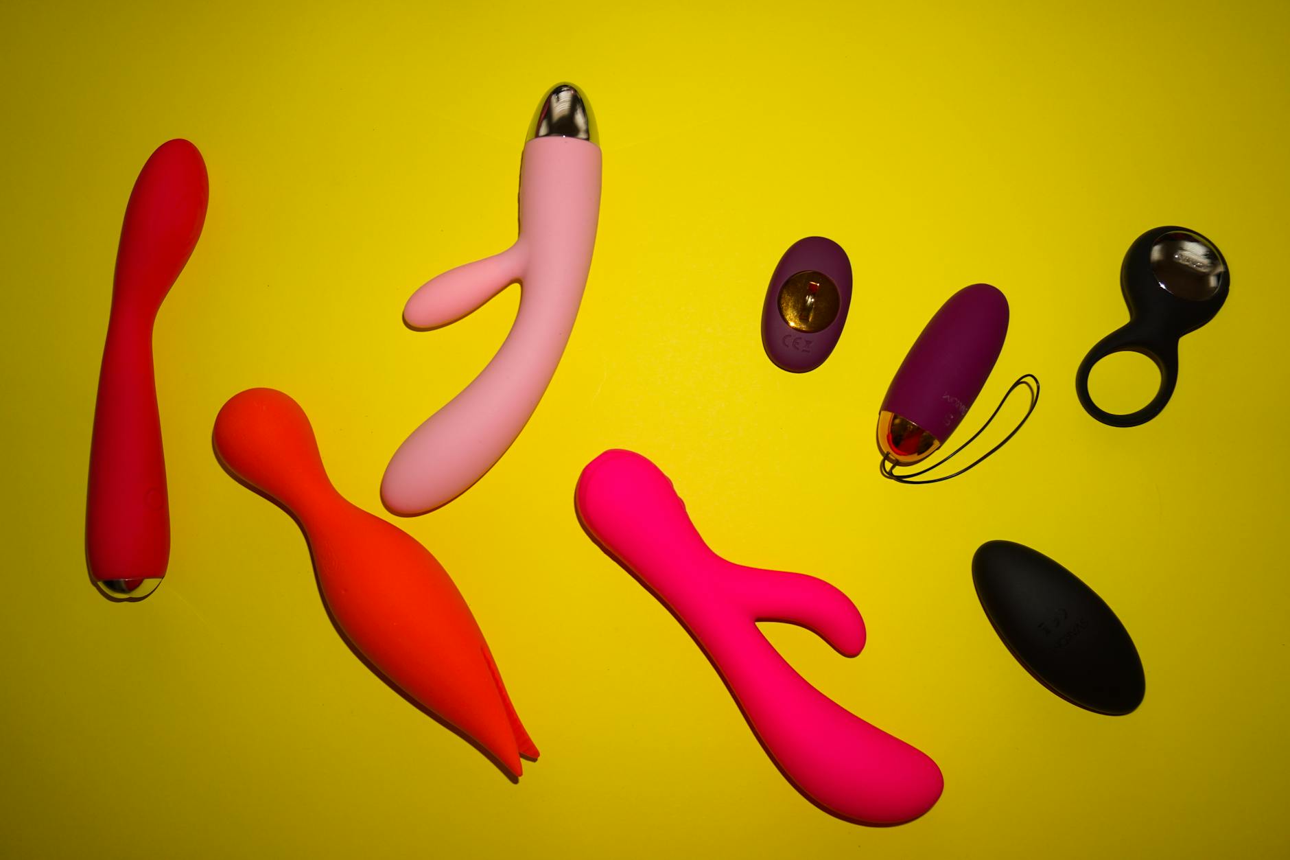 Vibrant arrangement of colorful sex toys on a bright yellow surface, representing diverse pleasure tools and intimate wellness